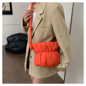 Detailed view of fashionable pleated puffy nylon crossbody bucket bag in bright orange color.