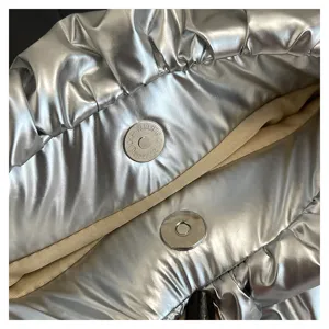 Detailed shot of silver metallic puffer handbag magnetic snap button, soft quilted fabric.