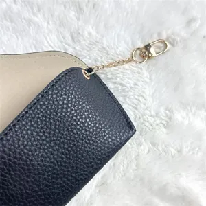 Detailed view of black textured leather glasses pouch with gold chain and clasp, fine stitching.