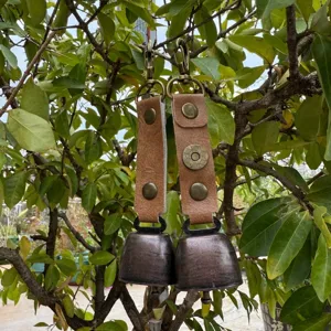 Outdoor bear bell close-up detail, vintage bronze metal finish with leather hanging strap.