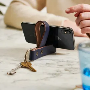 Leren telefoonstandaard sleutelhanger detail, minimalistisch blauw bureau accessoire.