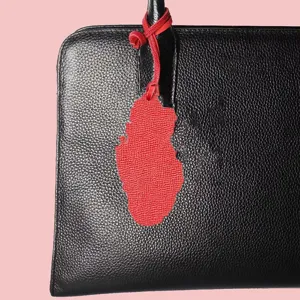 Close up detail of a black leather handbag featuring a red country map pendant accessory.