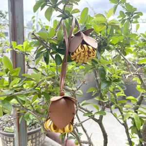 Vue détaillée du pendentif de sac en cuir fleur avec franges jaunes sur un arbre.