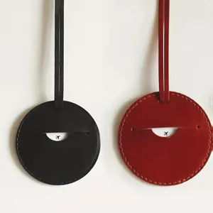 Étiquettes de bagages rondes en cuir noir et rouge avec lanière de suspension pour le voyage.