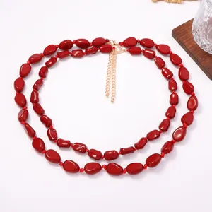 Dettaglio collana a doppio strato con perle ovali rosse irregolari e catenina dorata.
