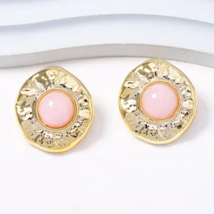 Nahaufnahme von vintage strukturierten goldfarbenen Ohrringen mit rosa Harzstein.