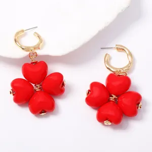 Detalle de pendientes de corazón rojo, joyería elegante para uso diario, acabado dorado.