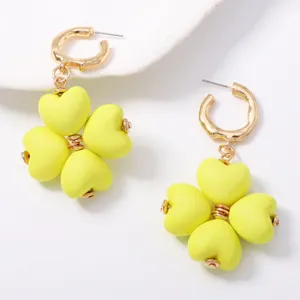 Vista detallada de pendientes de aro dorados con dijes en forma de flor de corazón amarillo.