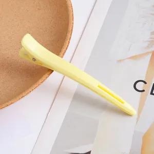 Yellow plastic hair salon styling clip, professional duckbill hair clamp detail view.