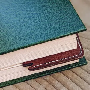 Close-up detail of a brown leather leaf bookmark with white stitching inserted in a book page.