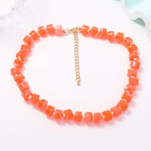Dettaglio collana di perle arancioni con sfere cilindriche sfumate e catenella di estensione.