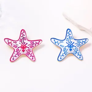 Dettaglio spilla stella marina in smalto con motivi floreali rosa e blu e bordo dorato.