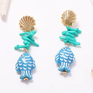Primo piano dettagliato di orecchini pendenti in ceramica con pesce e conchiglia marina.