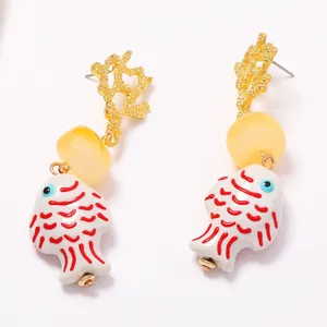 Primo piano dettagliato di orecchini pendenti in ceramica a forma di pesce con corallo dorato.