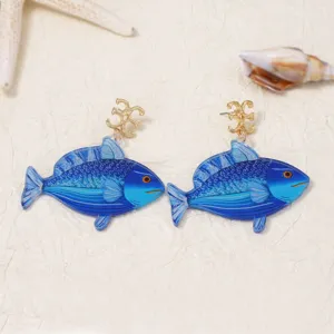 Primo piano di orecchini di pesce in acrilico blu con perni dorati, eleganti e unici nel design.