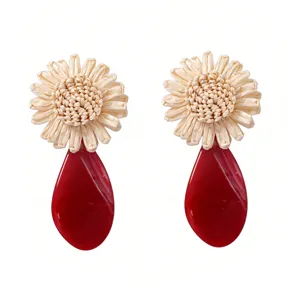 Close-up of woven raffia flower and glossy red acrylic teardrop earrings detail view.