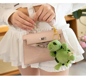 Detail view of a cute green turtle plush keychain hanging from a stylish pink handbag charm.