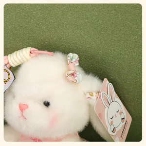 Gros plan détaillé d'un pendentif lapin en peluche blanche avec nœud floral et texture duveteuse.