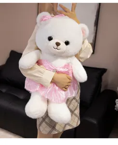 Detailed view of cute white plush teddy bear wearing pink sparkly dress and bow.