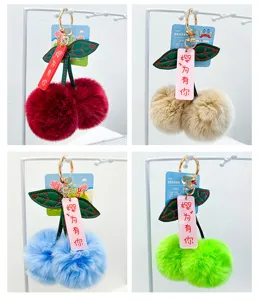 Plush cherry keychain detail showing soft fluffy ball, green embroidered leaves and gold ring.