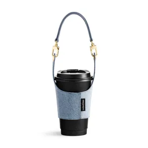 Denim coffee cup sleeve with detachable leather handle and gold hardware for portable use.