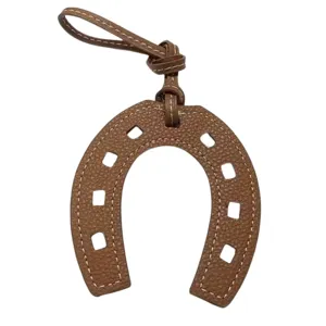 Nahaufnahme des braunen Leder Hufeisen Taschenanhängers mit feinen Nähten und Zubehör.