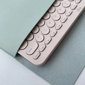 Close-up detail of a pink wireless keyboard with round keycaps inside a mint green PU leather case.