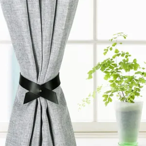 Detail view of black PU leather curtain tieback holding modern grey fabric curtain in room.