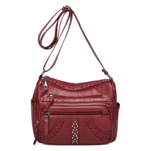 Red multi-compartment crossbody shoulder bag for women with studs and braided details.
