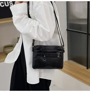 Detail view of black soft leather crossbody bag with multiple zipper pockets worn by model.