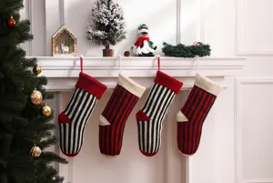Primo piano di quattro calze di Natale a righe in maglia appese a un camino bianco.
