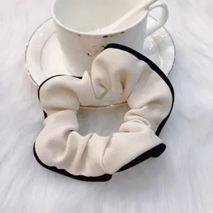 Detailed shot of elegant off-white fabric hair scrunchie with chic black contrast edge design.