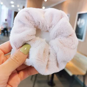 Primo piano di un morbido scrunchie per capelli in peluche rosa, con dettagli di texture invernale.