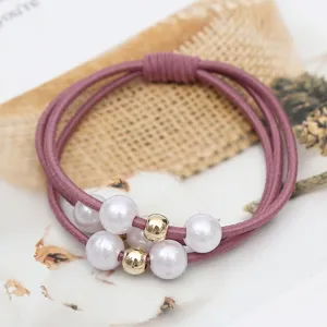 Detailed shot of a stylish pearl hair tie with gold beads, elastic rope for women styling.