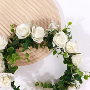Detail view of a white floral hair wreath, bridal flower crown with roses and green leaves.