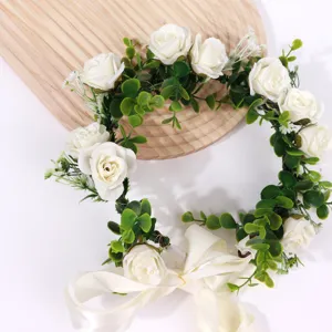 Close-up detail of white rose floral crown with green leaves and ribbon for wedding and party.