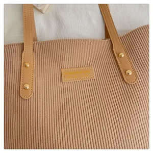Corduroy tote bag detail showing dual PU leather straps, metal rivets, and brand label.