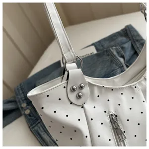 Close-up detail of white polka dot shoulder bag with metal zipper and rivet decor.