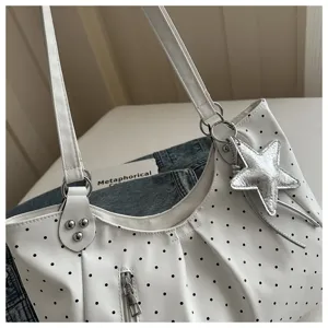 Detail view of white shoulder bag with black polka dots, silver star pendant and zipper pocket.