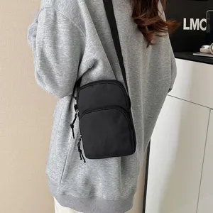 Detailed shot of a black minimalist crossbody bag worn on a model, showing dual zip pockets.