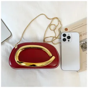 Red clutch bag with gold abstract handle and chain strap detail, stylish and modern accessory.