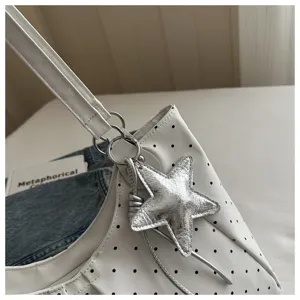 Close-up detail of white polka dot shoulder bag with stylish silver star pendant and hardware rings.