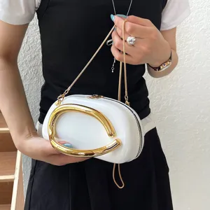 Close-up of elegant white oval handbag featuring sculptural gold metal handle and chain strap.