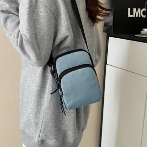 Detail shot of a light blue casual crossbody bag with black zippers and durable fabric strap.