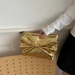 Gold metallic bow clutch bag closeup showcasing the shiny texture and elegant evening party style.