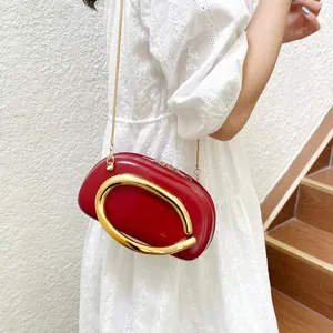 Detail view of a stylish red crossbody bag with a striking gold ring handle and chain strap.