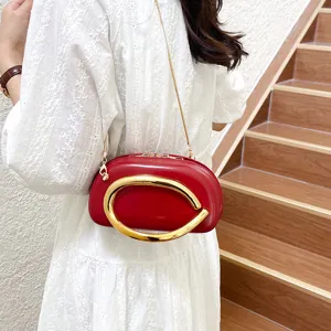 Red leather shoulder bag featuring a bold large gold metal handle and chain strap detail.