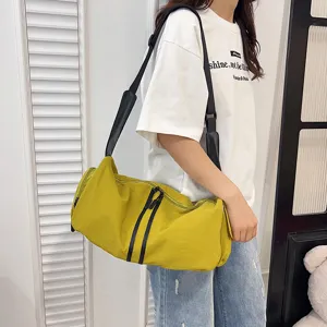 Detail shot of a casual yellow cylinder duffel bag with black straps worn by a model.