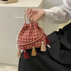 Close-up detail of red woven tweed drawstring pouch bag featuring delicate decorative tassels.
