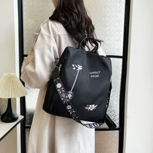 Detail view of stylish black nylon backpack featuring delicate floral embroidery and letters.
